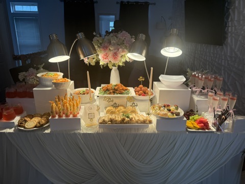 A full grazing and drinks display table with florals, warm lamps and small chops